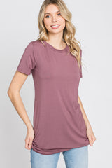 woman wearing a mauve short sleeve top with a relaxed fit and side ruching, paired with light blue jeans