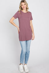 woman wearing a mauve short sleeve tunic top and light blue skinny jeans, posing with one hand on her hip