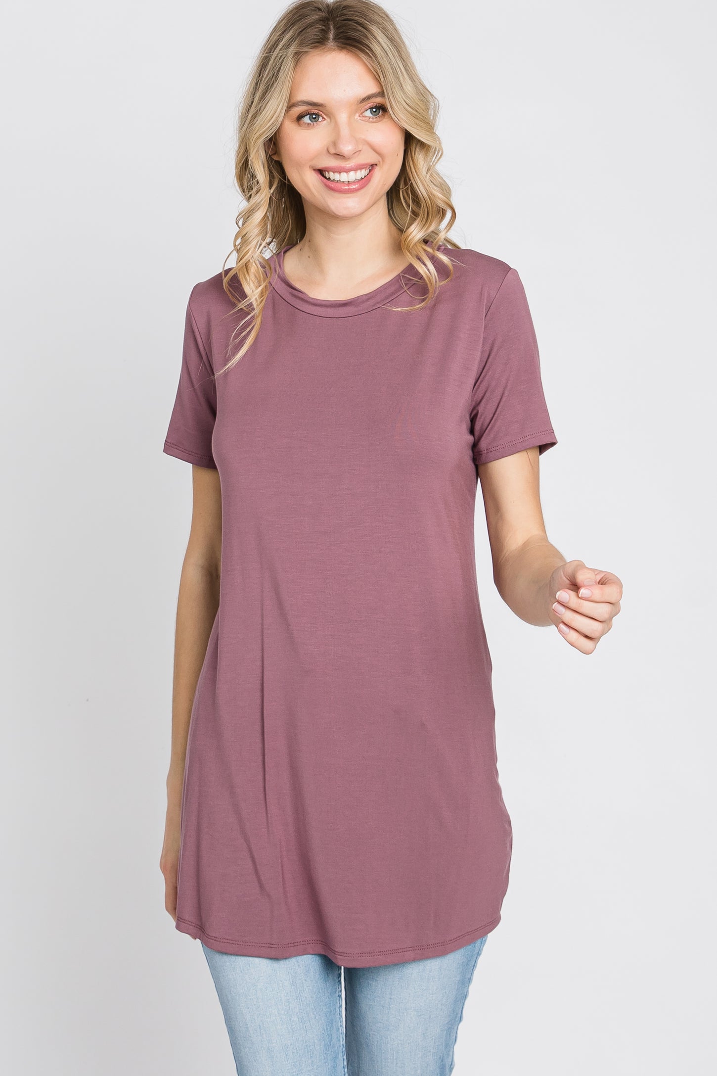 woman wearing a mauve short sleeve tunic top and light wash jeans against a white background