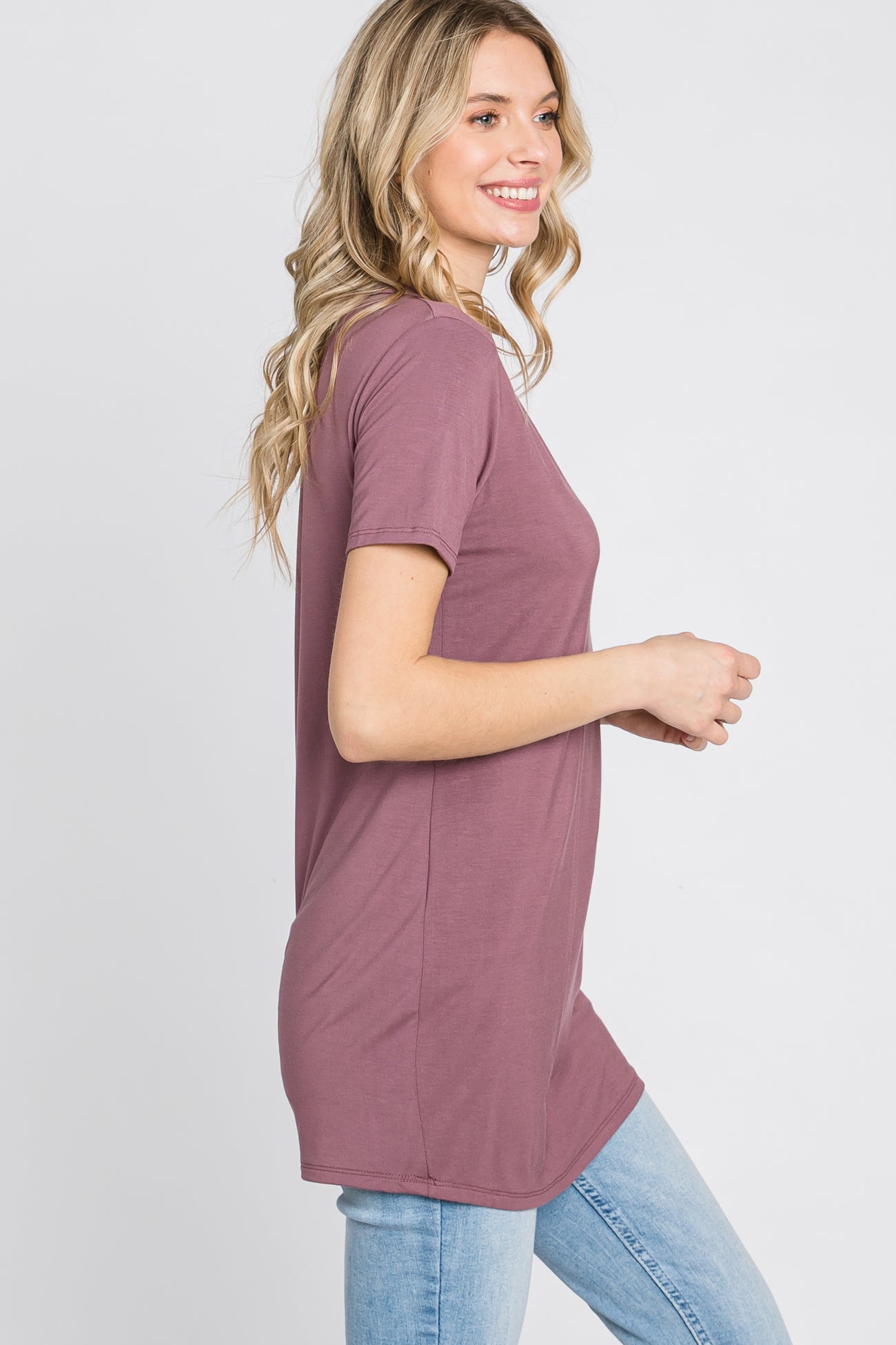 woman wearing a slim-fit mauve t-shirt with short sleeves and a rounded hem, paired with light blue jeans