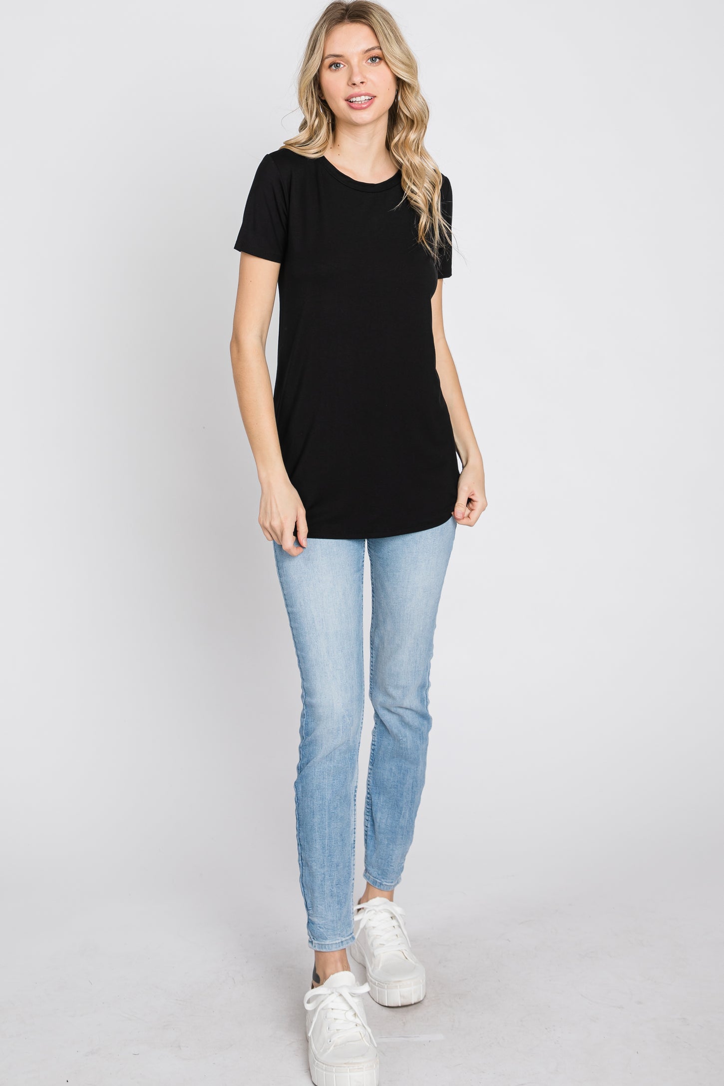 woman wearing a black short sleeve t-shirt and light blue skinny jeans, standing against a white background