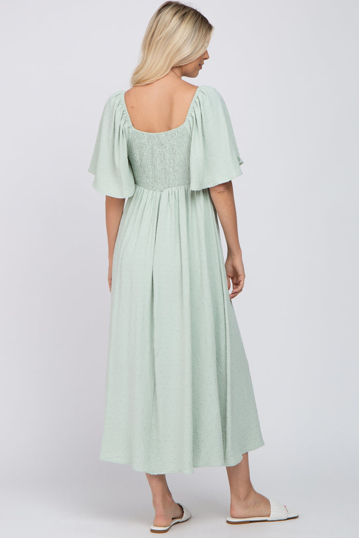 woman wearing a mint green midi dress with flutter sleeves and a smocked back detail