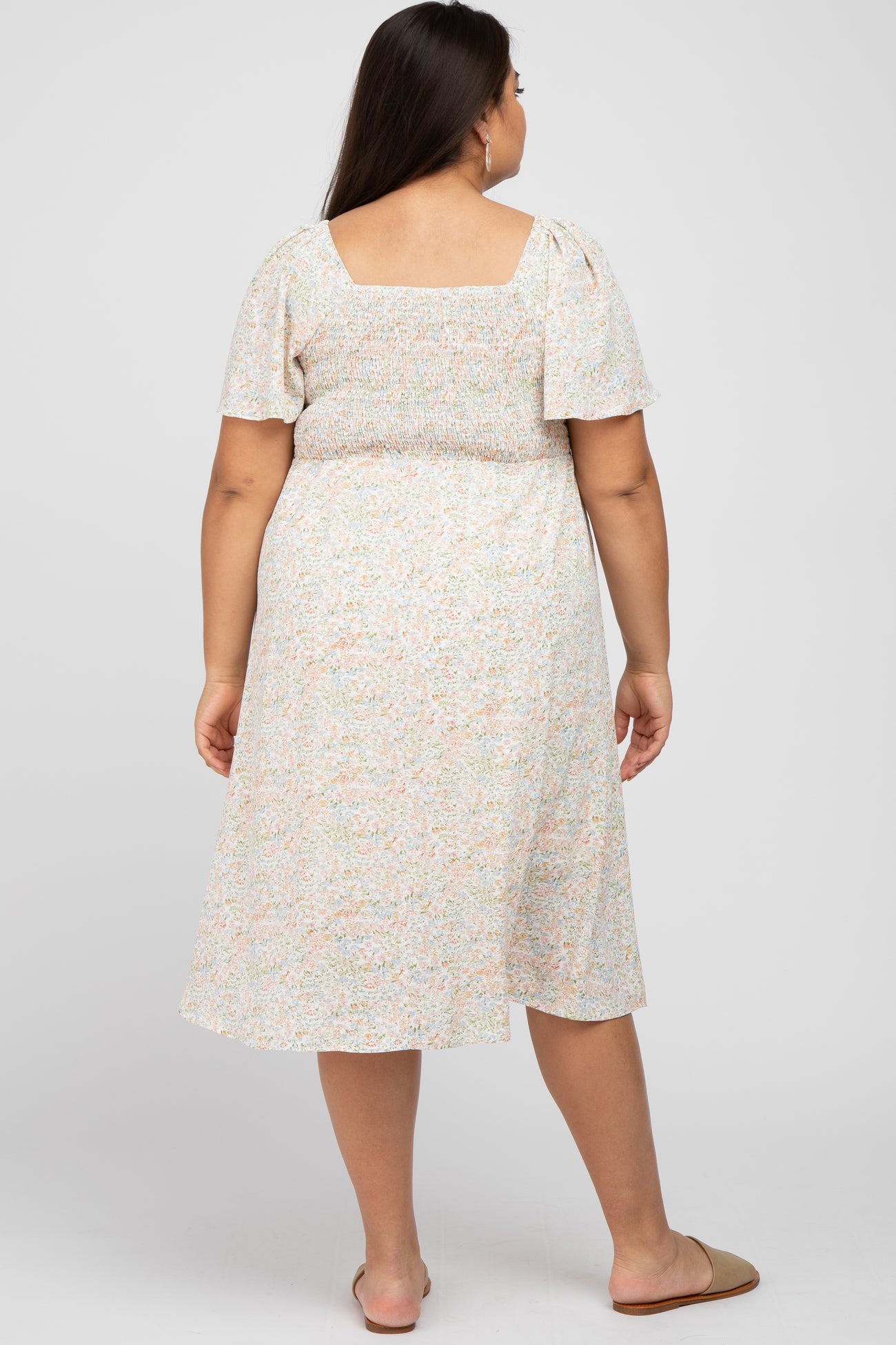 woman wearing a floral print plus-size midi dress with short sleeves and a smocked bodice, viewed from the back