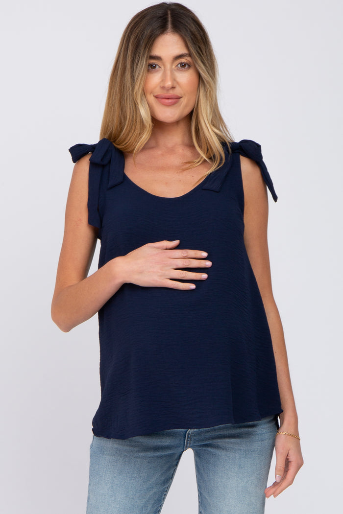 woman wearing a navy blue maternity top with tie shoulder details and holding her baby bump