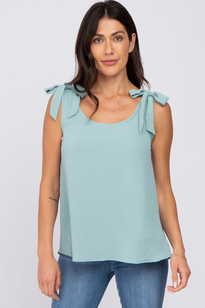 woman wearing a light blue sleeveless top with bow tie details on the shoulders and paired with denim jeans