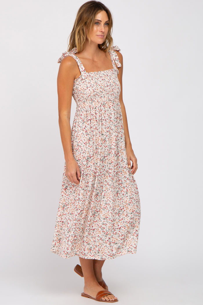 woman wearing a midi-length floral dress with tied shoulder straps and a smocked bodice, paired with tan slide sandals
