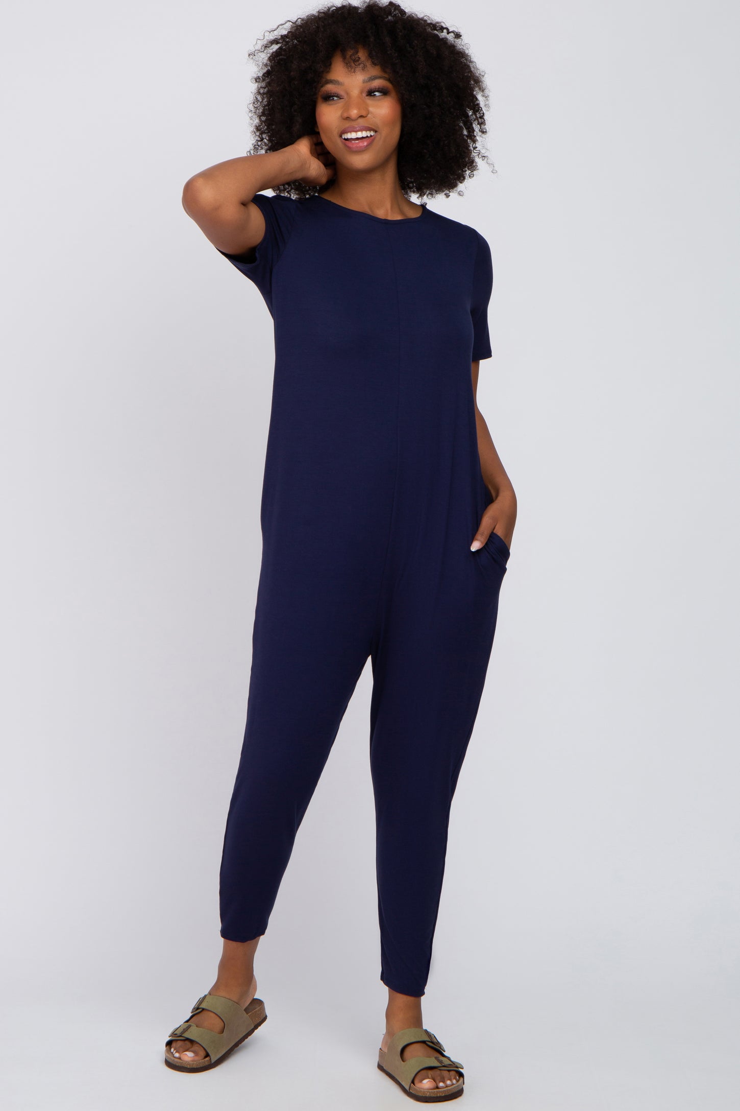 woman wearing a navy blue short sleeve jumpsuit with side pockets and relaxed fit sandals