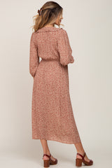 woman wearing a rust-colored floral maternity maxi dress with long sleeves and a cinched waist, showing her baby bump