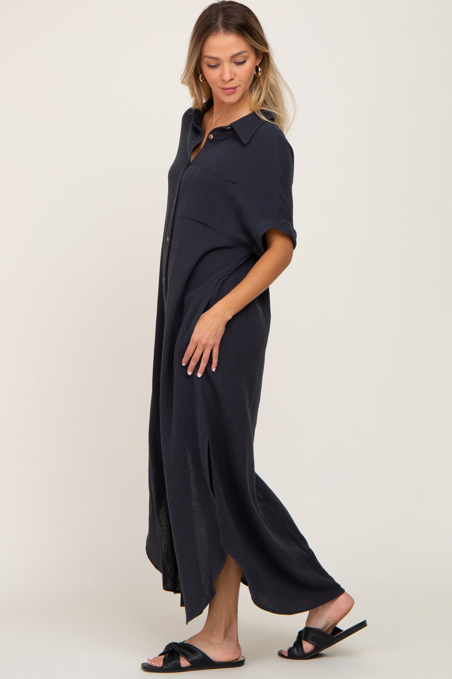 woman wearing a navy blue button-up maxi dress with short sleeves and side slits, standing in profile
