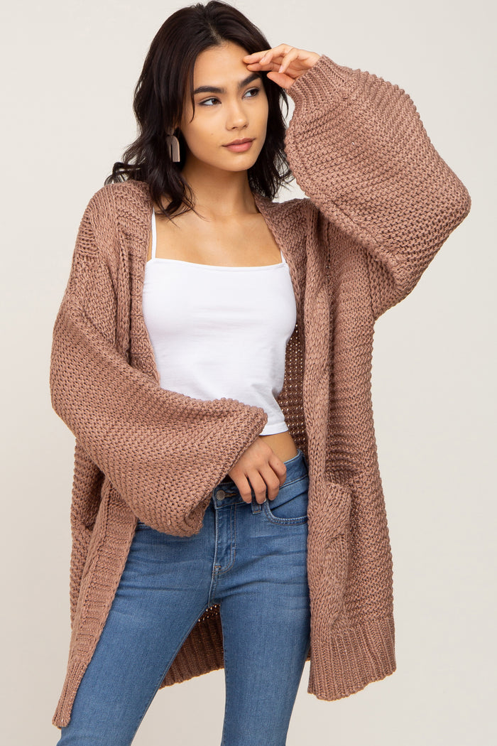 Woman wearing a mauve oversized chunky knit cardigan with bell sleeves, white tank top, and blue jeans