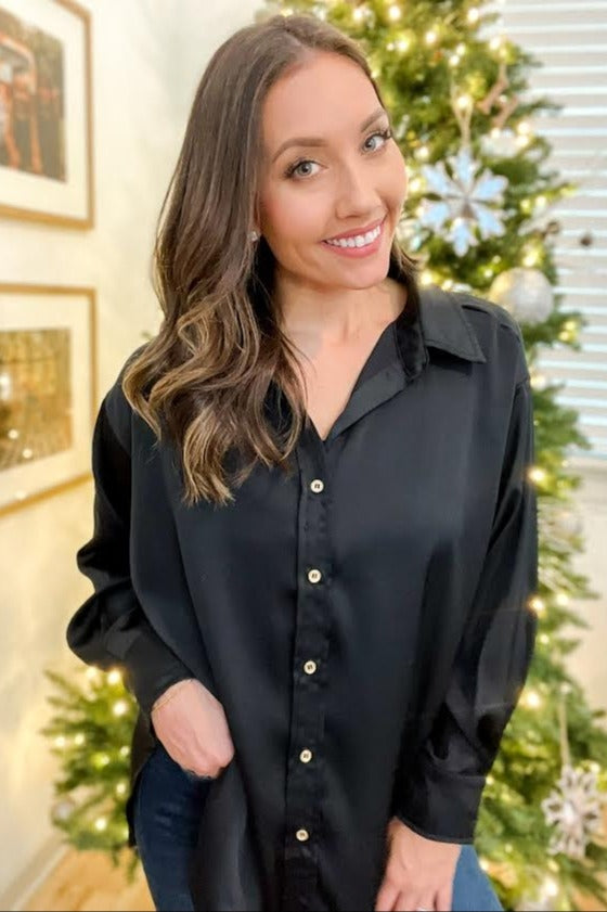 smiling woman wearing a black satin button-down shirt standing in front of a decorated Christmas tree