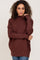 woman wearing a brown oversized sweater with a cowl neck and long sleeves, posing with one hand on her shoulder