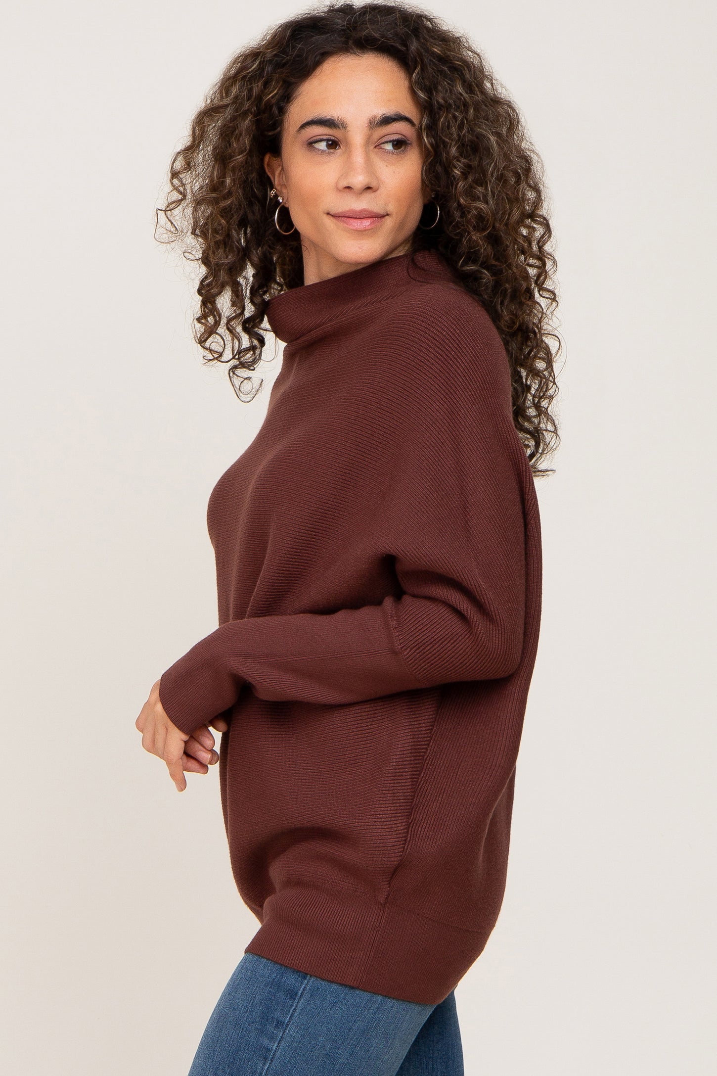 woman wearing a brown oversized sweater with a turtleneck and long sleeves, styled with blue jeans