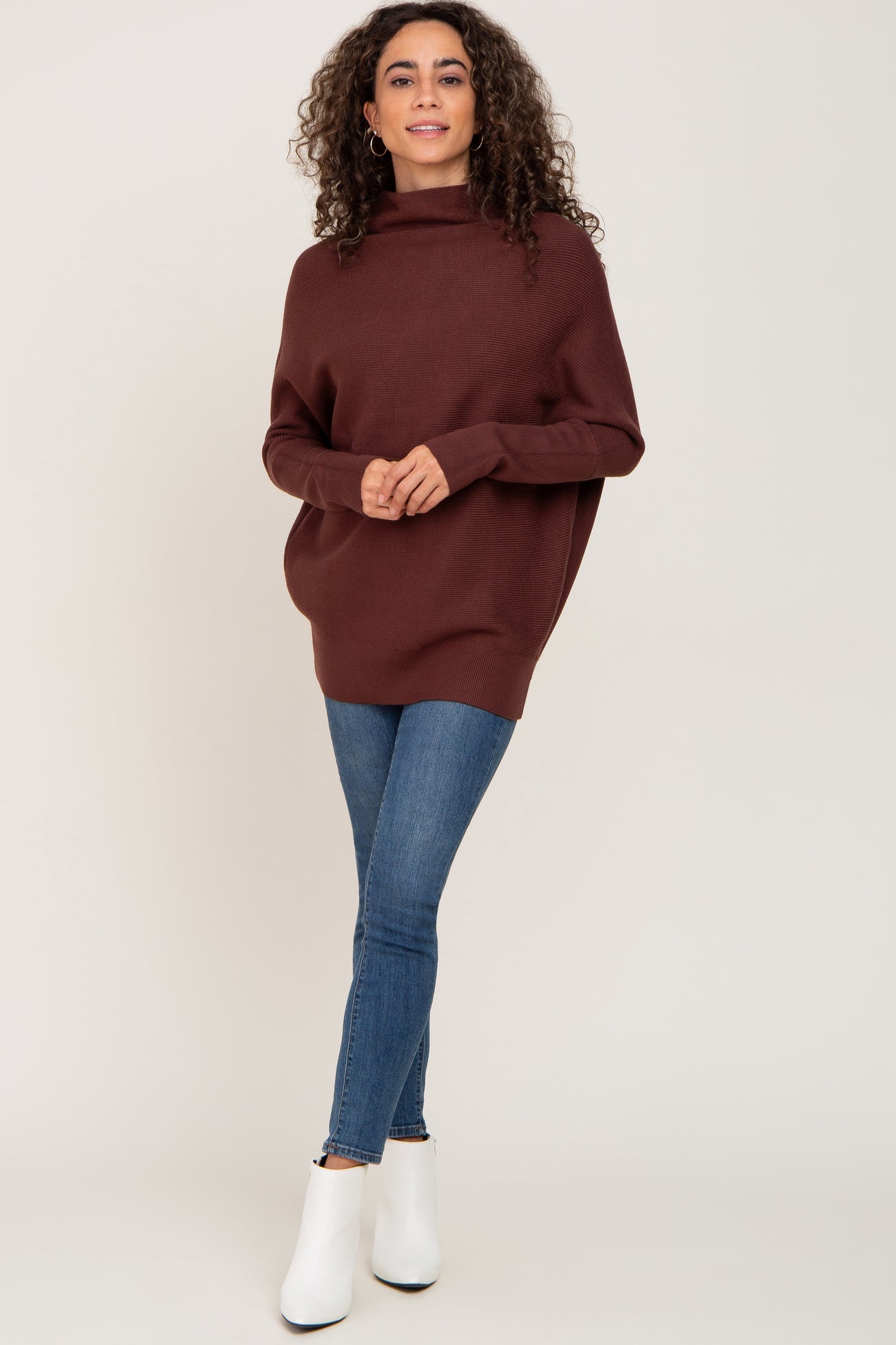 woman wearing a brown oversized sweater with a cowl neck and skinny jeans, paired with white ankle boots