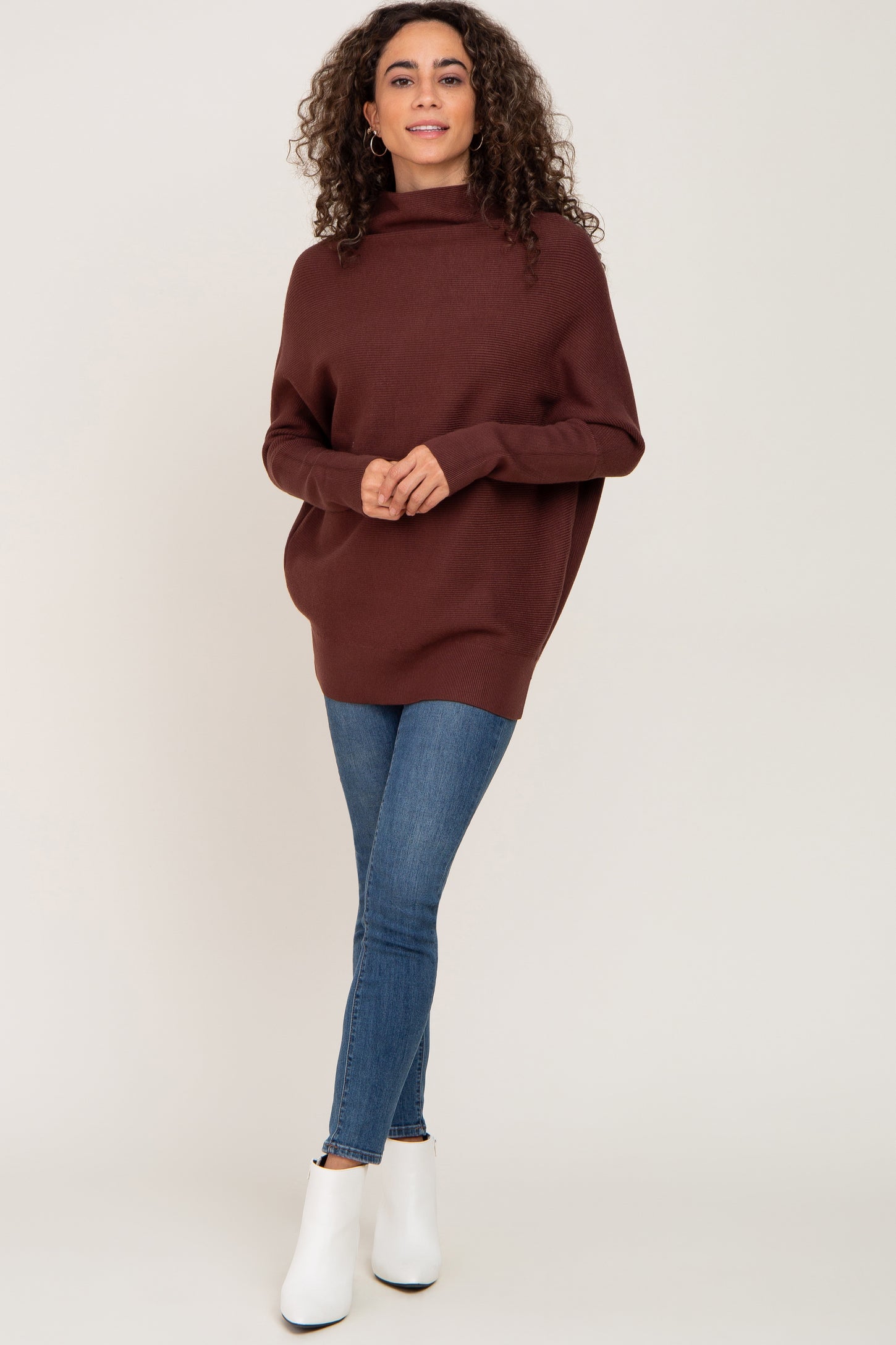 woman wearing a brown oversized sweater with a cowl neck and skinny jeans, paired with white ankle boots