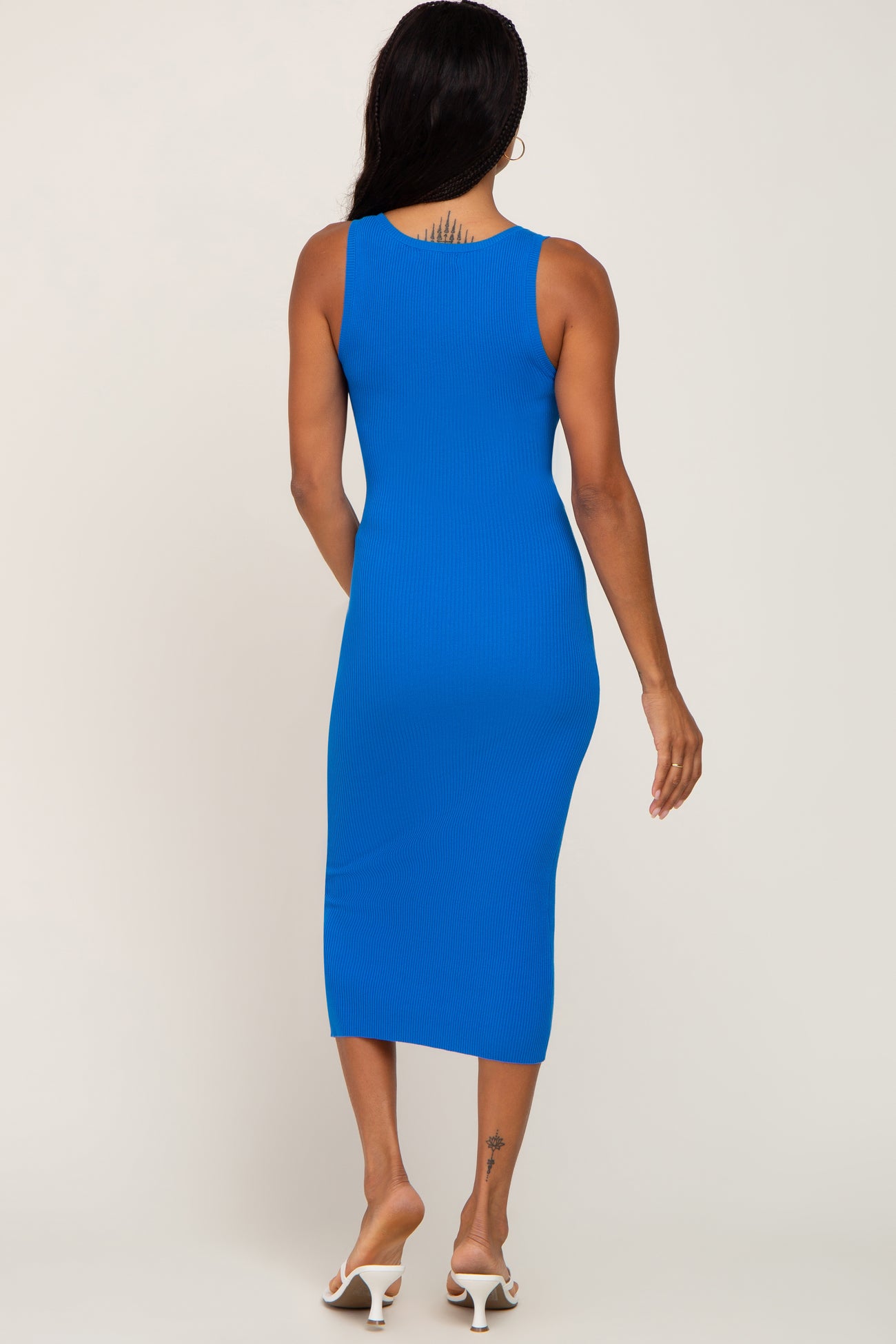 woman wearing a fitted royal blue ribbed midi dress, viewed from the back, styled with white strappy sandals
