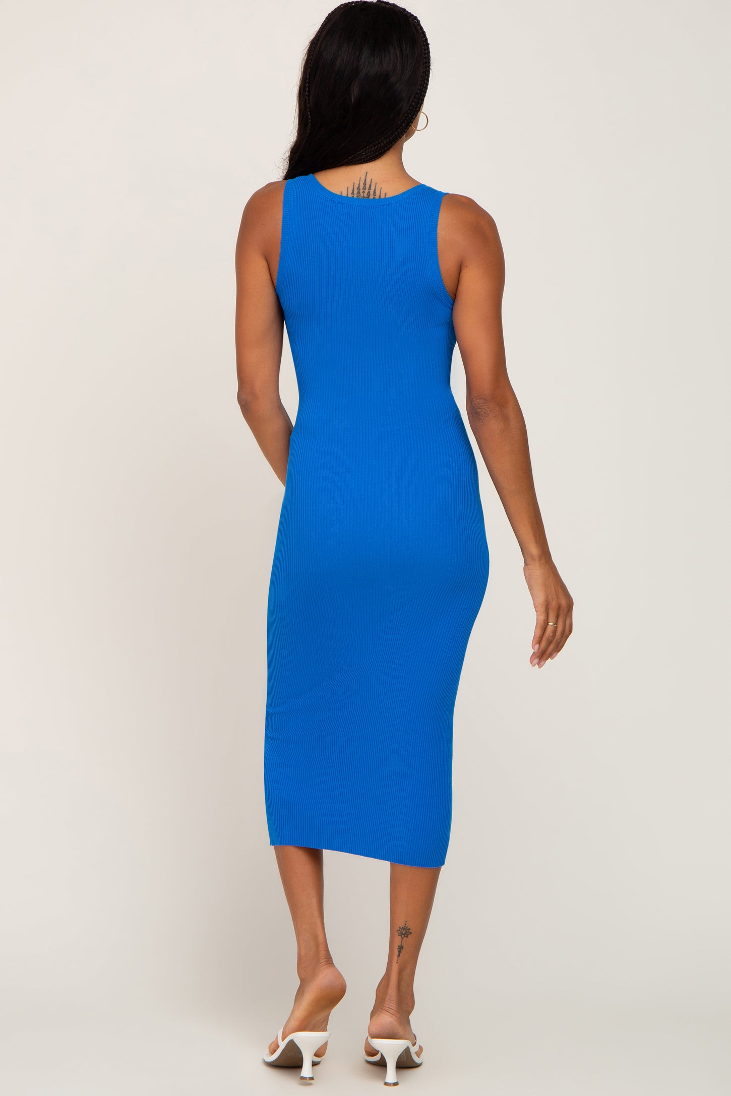 woman wearing a fitted royal blue ribbed midi dress, viewed from the back, styled with white strappy sandals