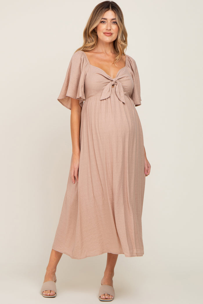 woman wearing a blush pink maternity dress with a tie front detail and flowing sleeves, highlighting her baby bump