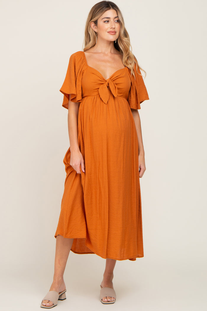 woman wearing an orange maternity dress with a tied front and flutter sleeves, showcasing her baby bump