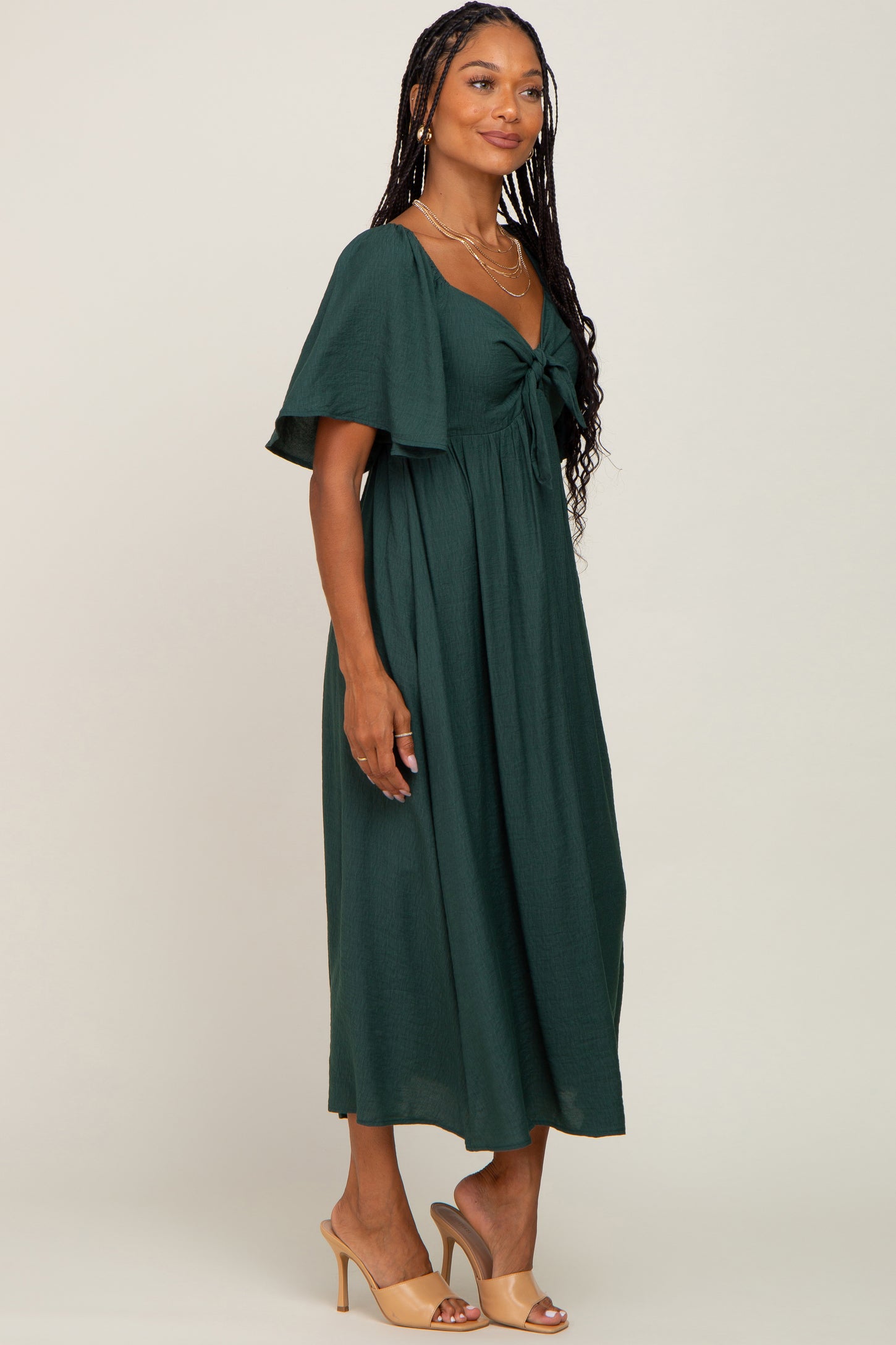 woman wearing a dark green maxi dress with a tie front and flutter sleeves, standing sideways with a neutral background