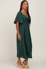 woman wearing a dark green maxi dress with a tie front and flutter sleeves, standing sideways with a neutral background
