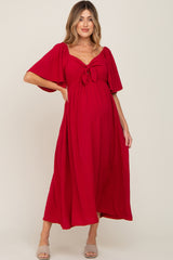 woman wearing a red maternity maxi dress with a tie front detail and short flutter sleeves, showcasing a visible baby bump