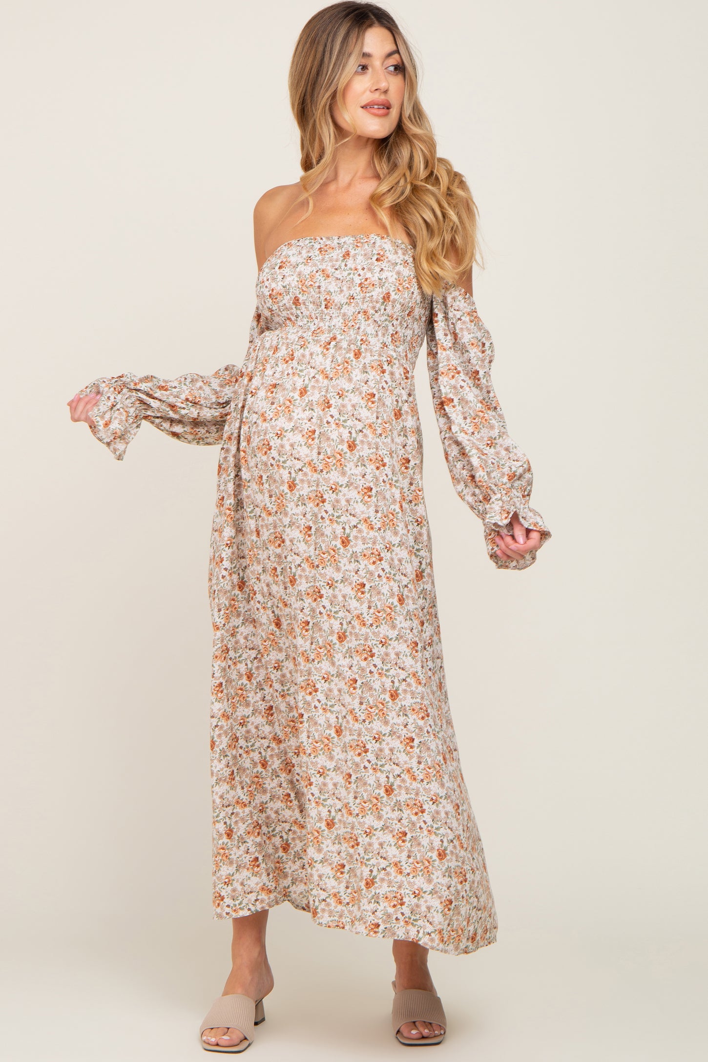woman wearing a floral off-shoulder maternity maxi dress with long sleeves and a baby bump visible