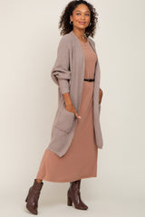 woman wearing a taupe long cardigan over a mauve maxi dress with a belt and brown ankle boots