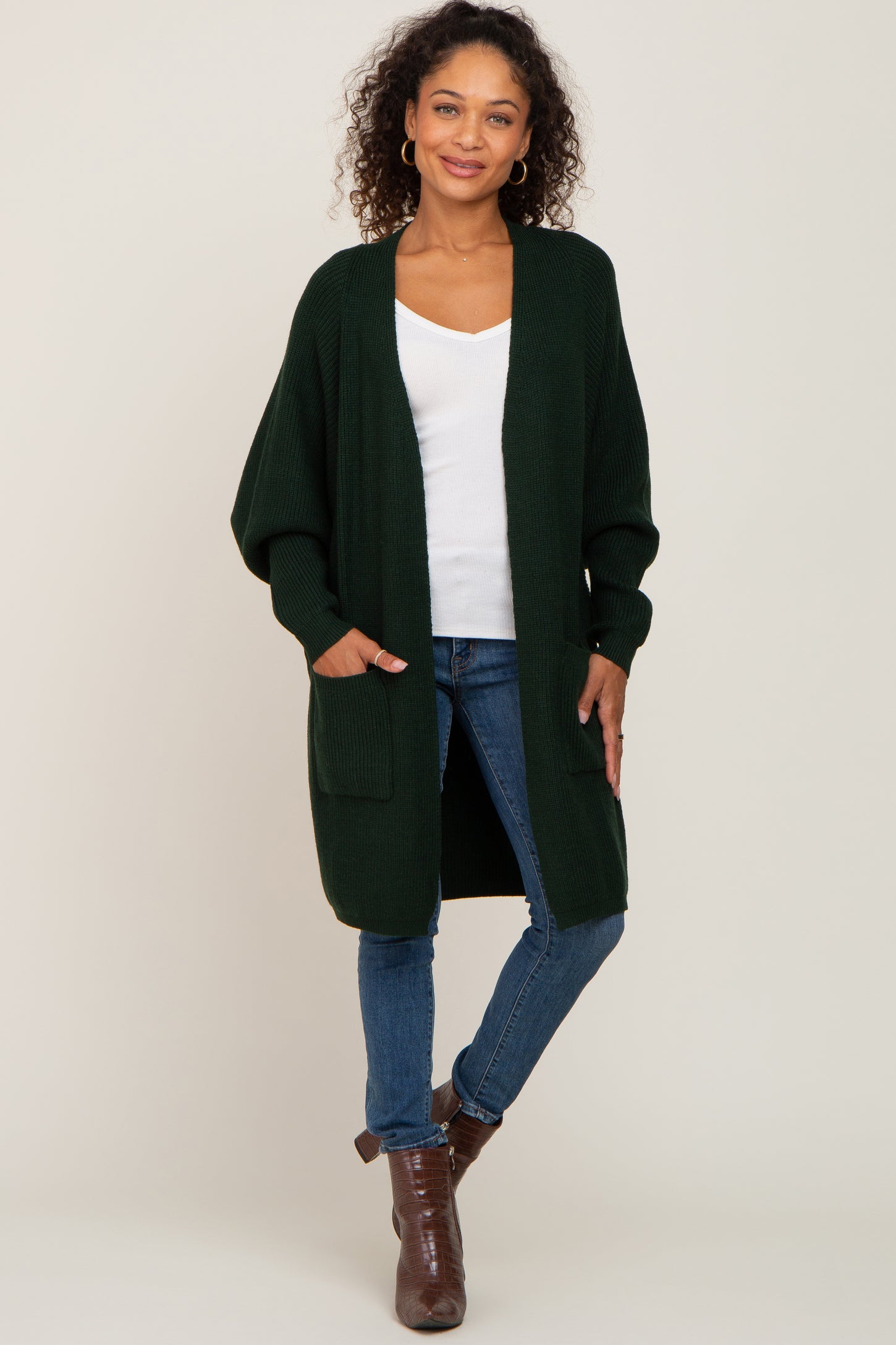 woman wearing a dark green long cardigan with pockets, paired with a white top and blue jeans