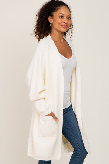 woman wearing a cream long cardigan with oversized sleeves and front pockets over a white tank top and blue jeans