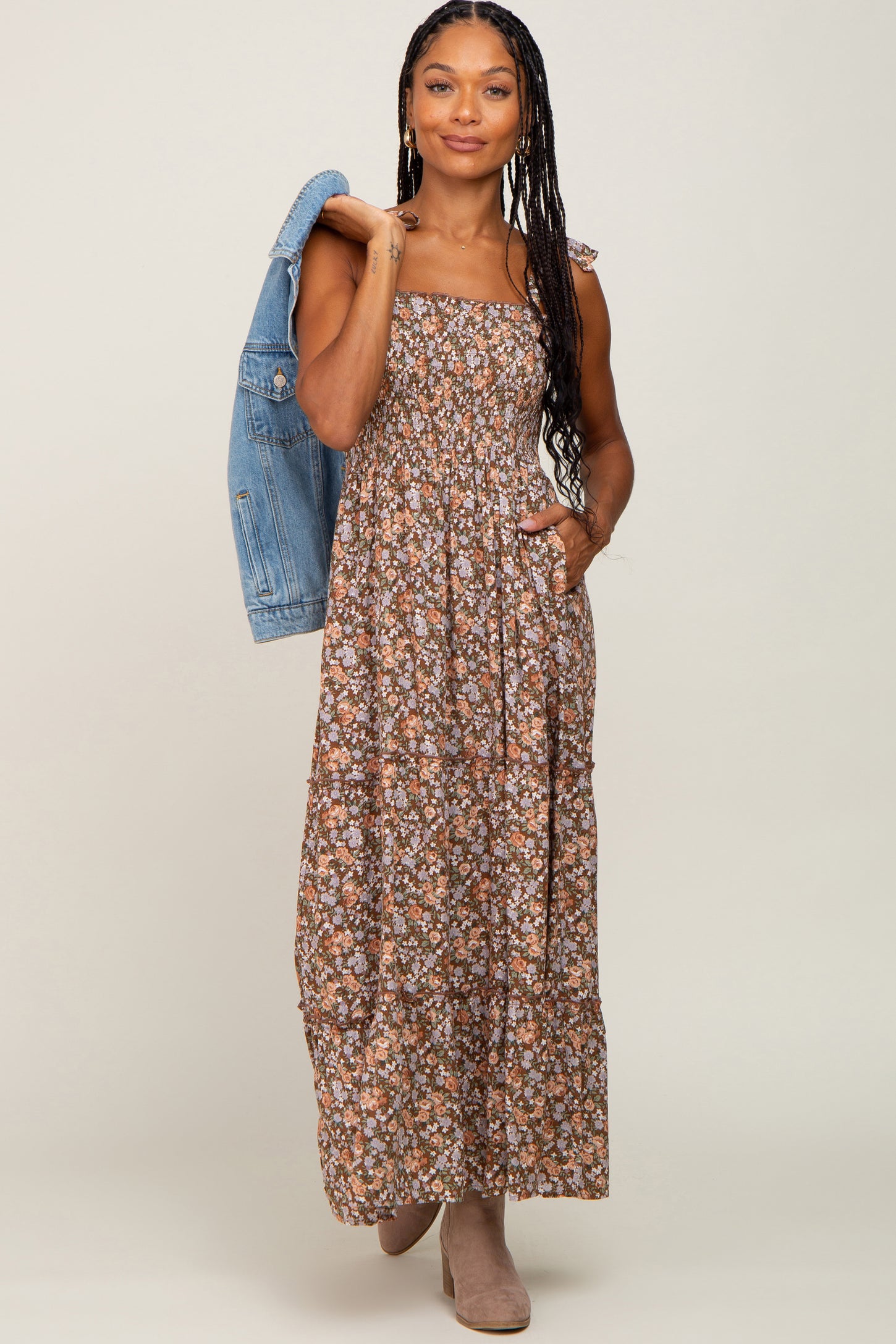 woman wearing a brown floral maxi dress with spaghetti straps and pockets, paired with a denim jacket and ankle boots