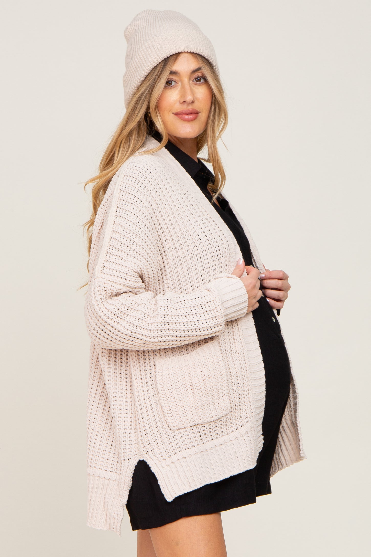 woman wearing a light pink maternity cardigan and matching beanie, with a visible baby bump