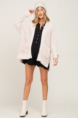 woman wearing a light pink oversized knit maternity cardigan with pockets and a black dress, showing her baby bump