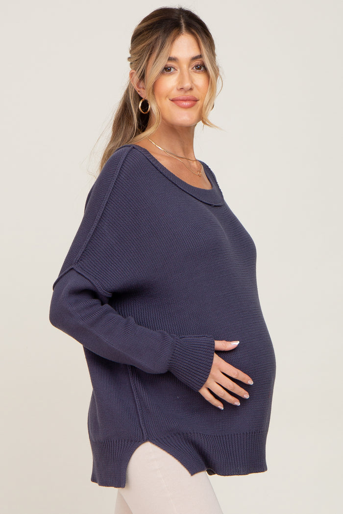 woman wearing a navy maternity sweater with a loose fit and side slits, gently cradling her baby bump