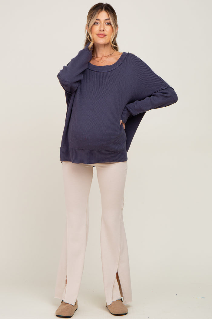 woman wearing a navy blue oversized maternity sweater and cream-colored flared pants, showing her baby bump