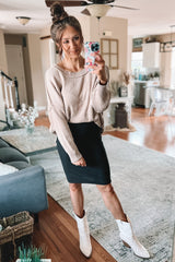 woman wearing a light beige oversized sweater and a black pencil skirt, paired with white ankle boots