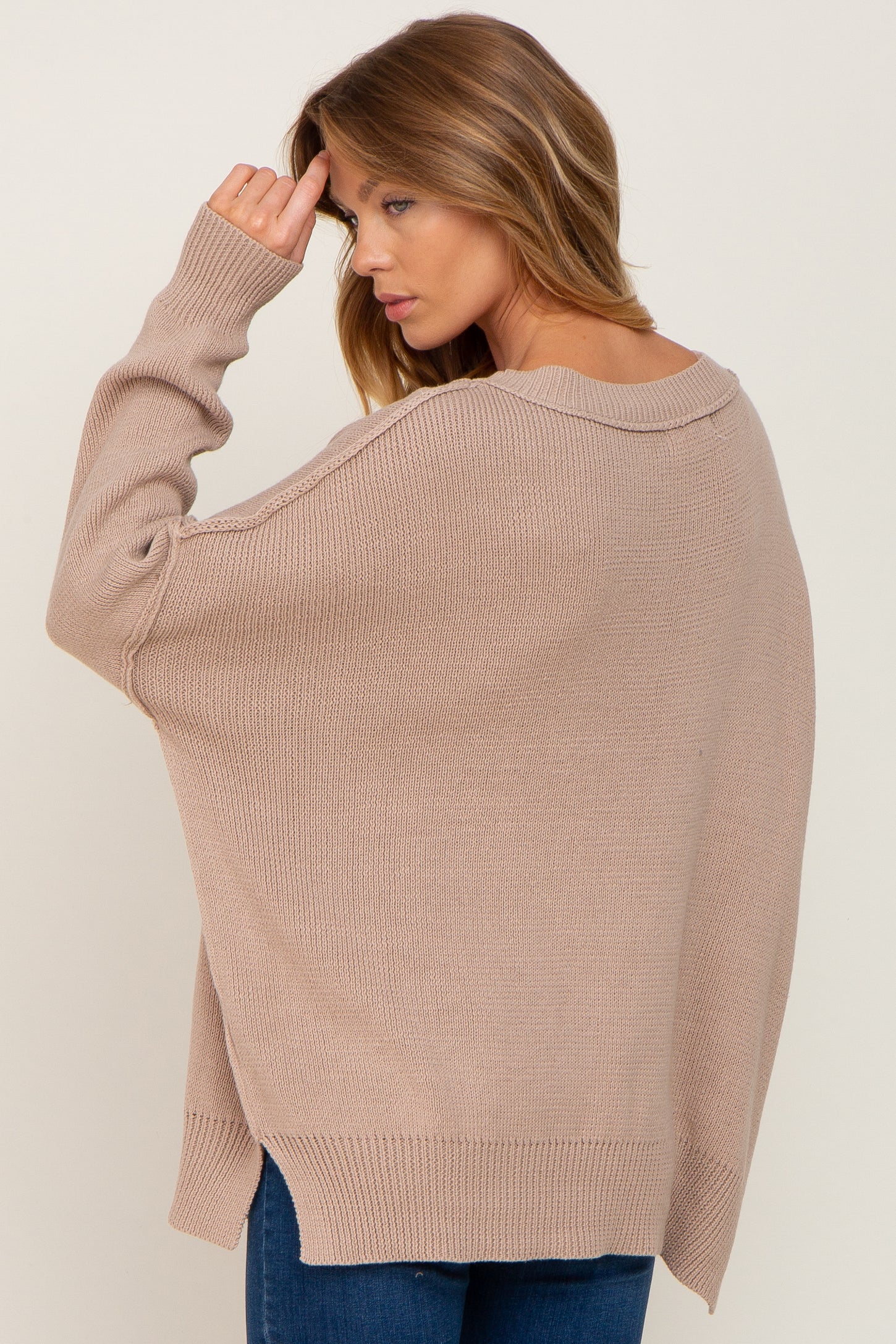 woman wearing a beige oversized sweater with a wide neckline and drop shoulders, styled with blue jeans