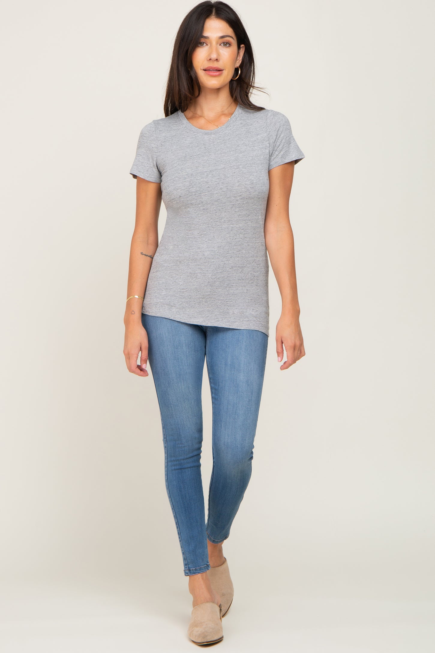 woman wearing a gray short sleeve tee and skinny jeans, standing and smiling at the camera