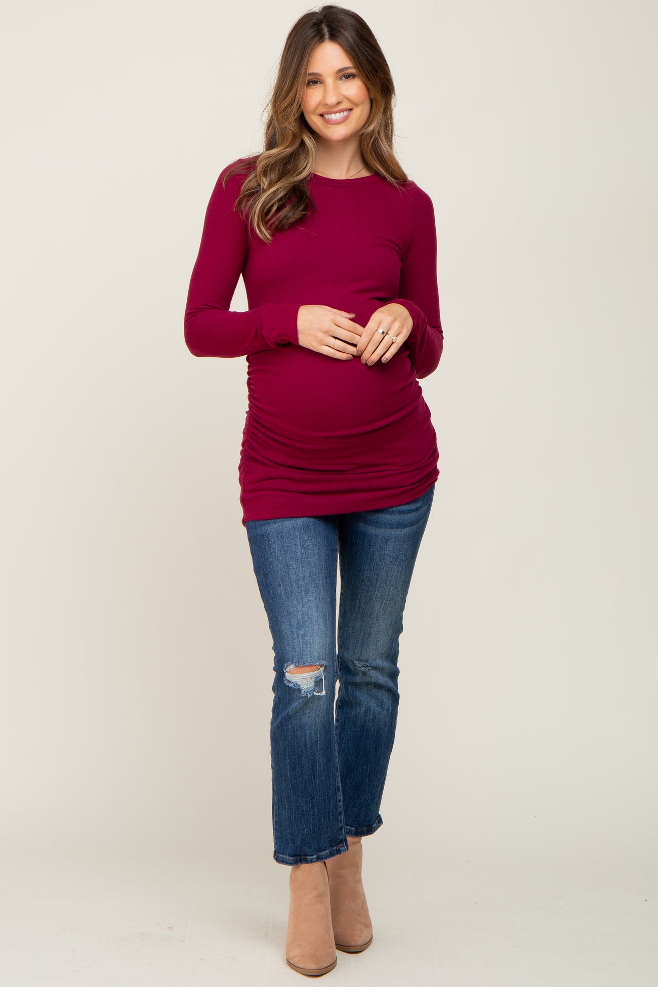 woman wearing a burgundy long sleeve maternity top, showing her baby bump, paired with distressed jeans and beige ankle boots