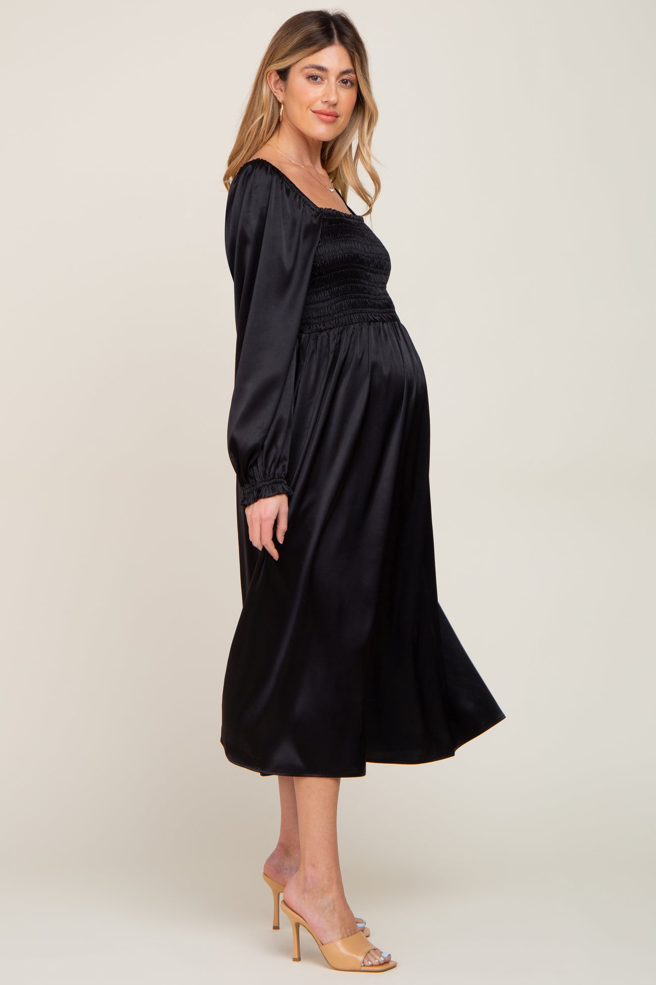 woman wearing a black satin maternity dress with smocked bodice and long sleeves, showcasing her baby bump