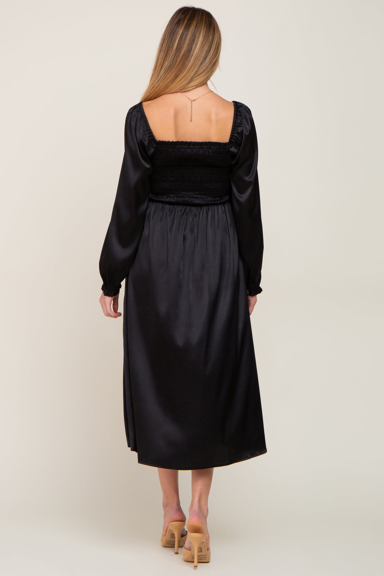 woman wearing a black satin maternity dress with a smocked bodice and long sleeves, shown from the back
