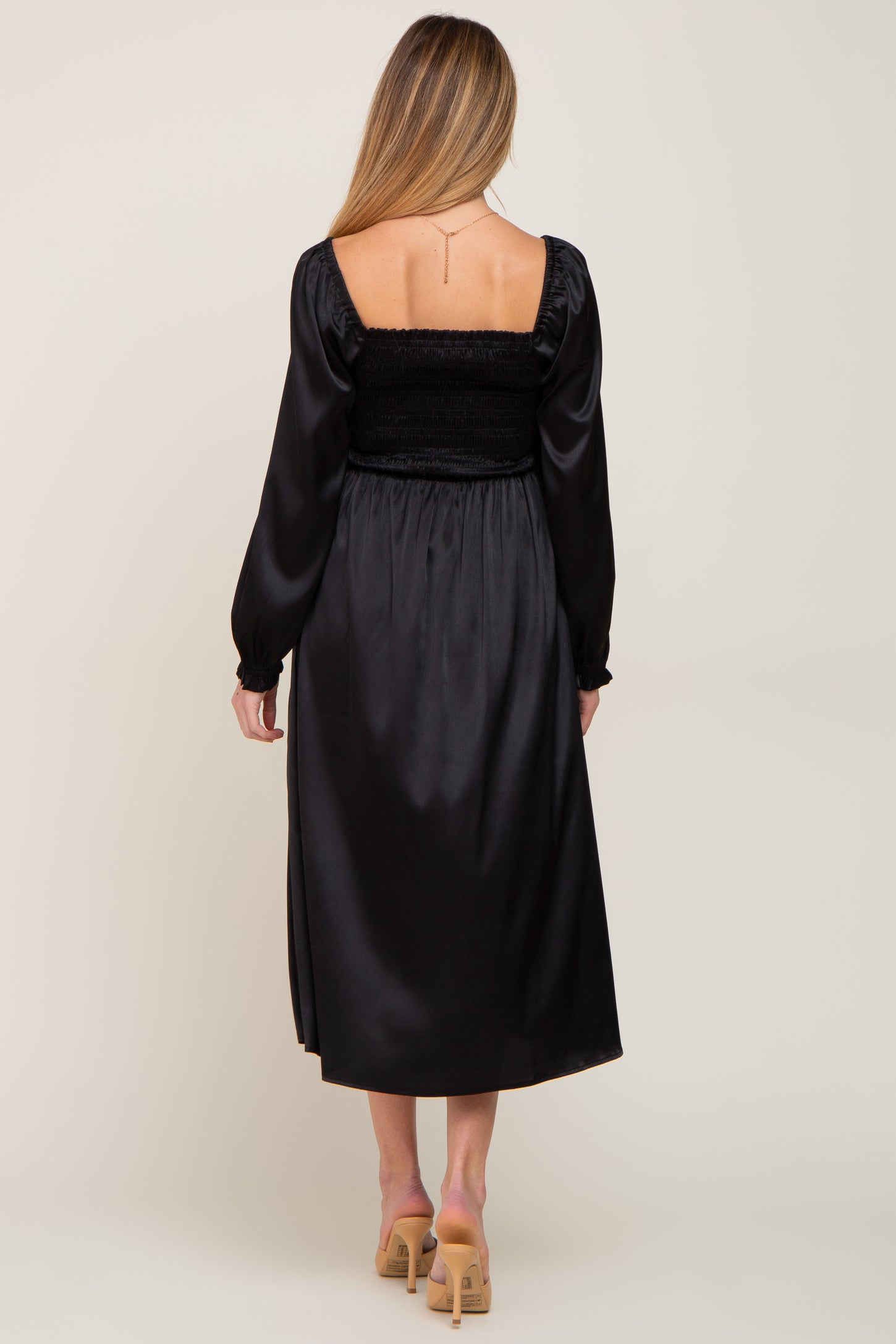 woman wearing a black satin maternity dress with a smocked bodice and long sleeves, shown from the back