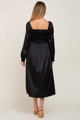woman wearing a black satin maternity dress with a smocked bodice and long sleeves, shown from the back