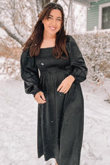 woman wearing a black smocked long sleeve dress, standing in the snow with a smiling expression