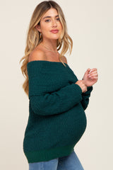 woman wearing a dark green off-the-shoulder maternity sweater with long sleeves and a visible baby bump