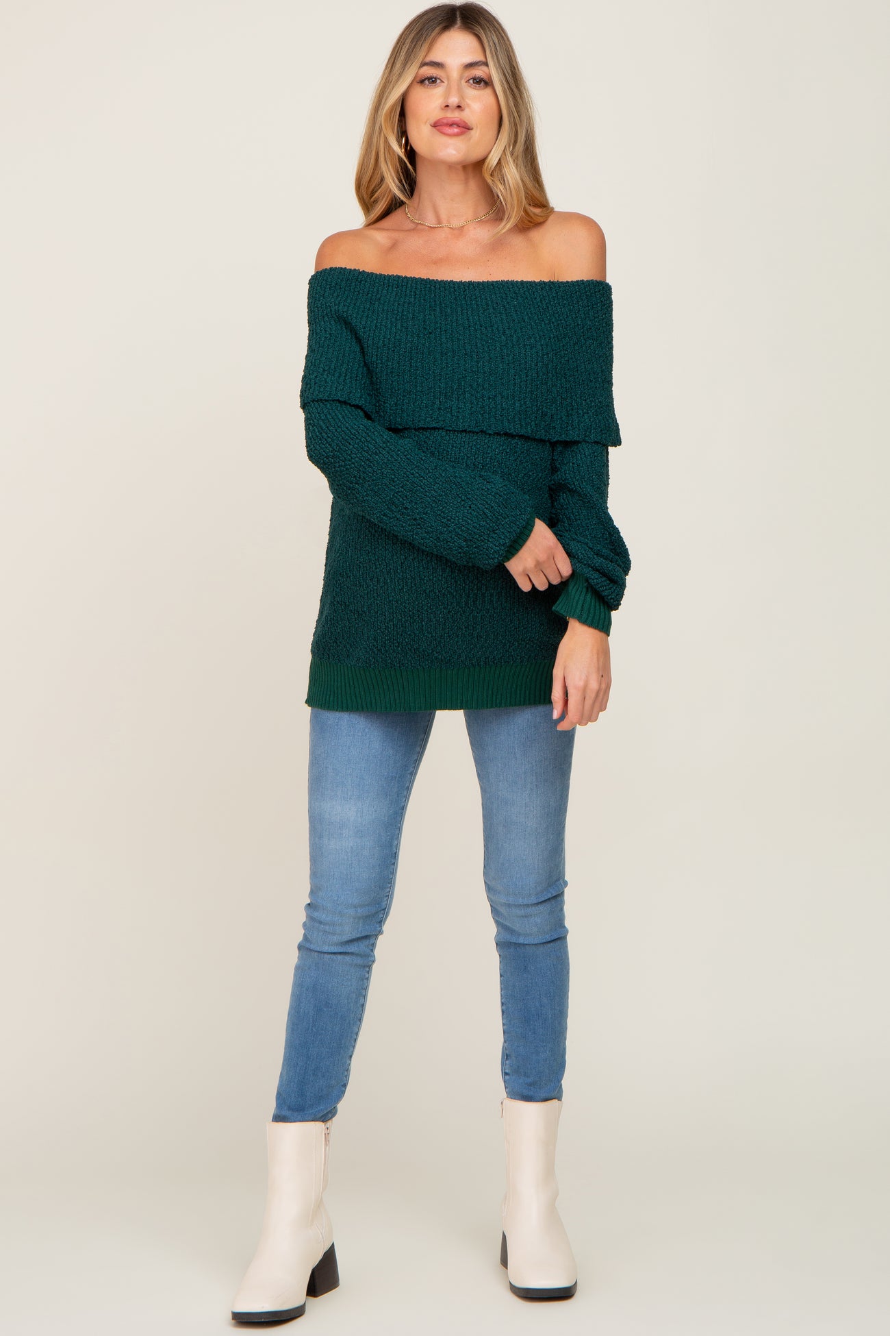 woman wearing a dark green off-the-shoulder maternity sweater paired with skinny jeans and ankle boots