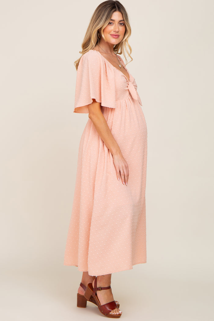 woman wearing a blush pink maternity dress with short flutter sleeves and a bow detail, showing her baby bump