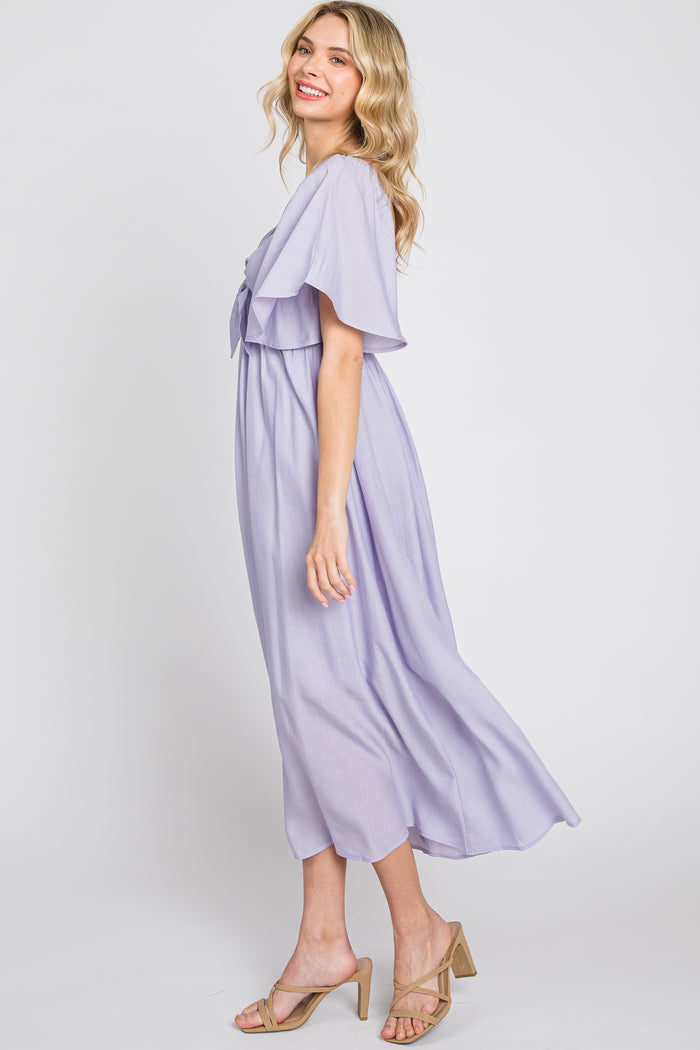 woman wearing a lavender maxi dress with flutter sleeves and a tie waist, standing sideways with a smile