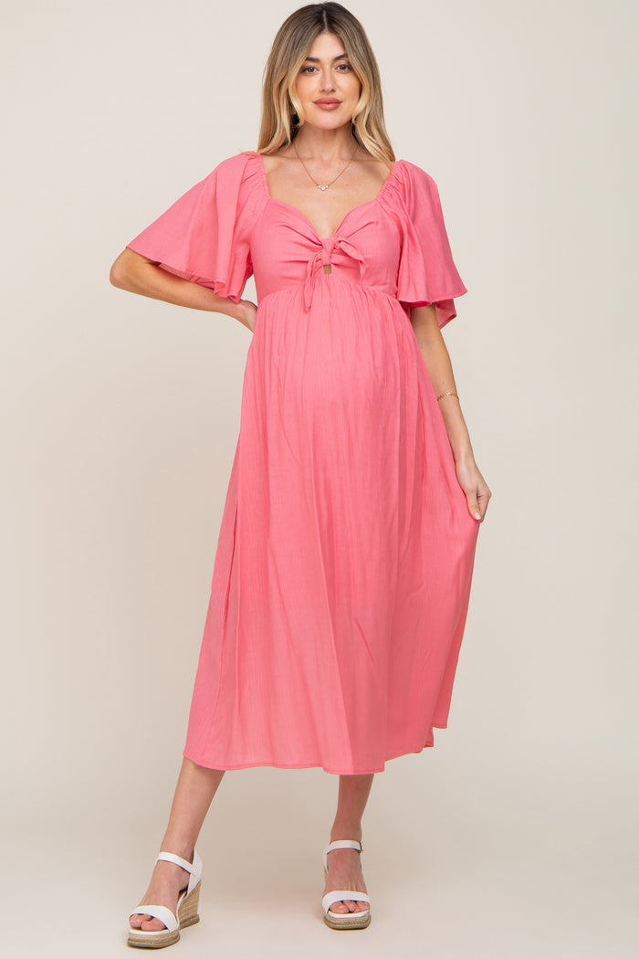 woman wearing a pink maternity dress with short flutter sleeves and a tie front, showcasing her baby bump