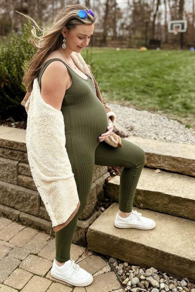 pregnant woman in olive green ribbed jumpsuit and white sneakers posing outdoors on stone steps